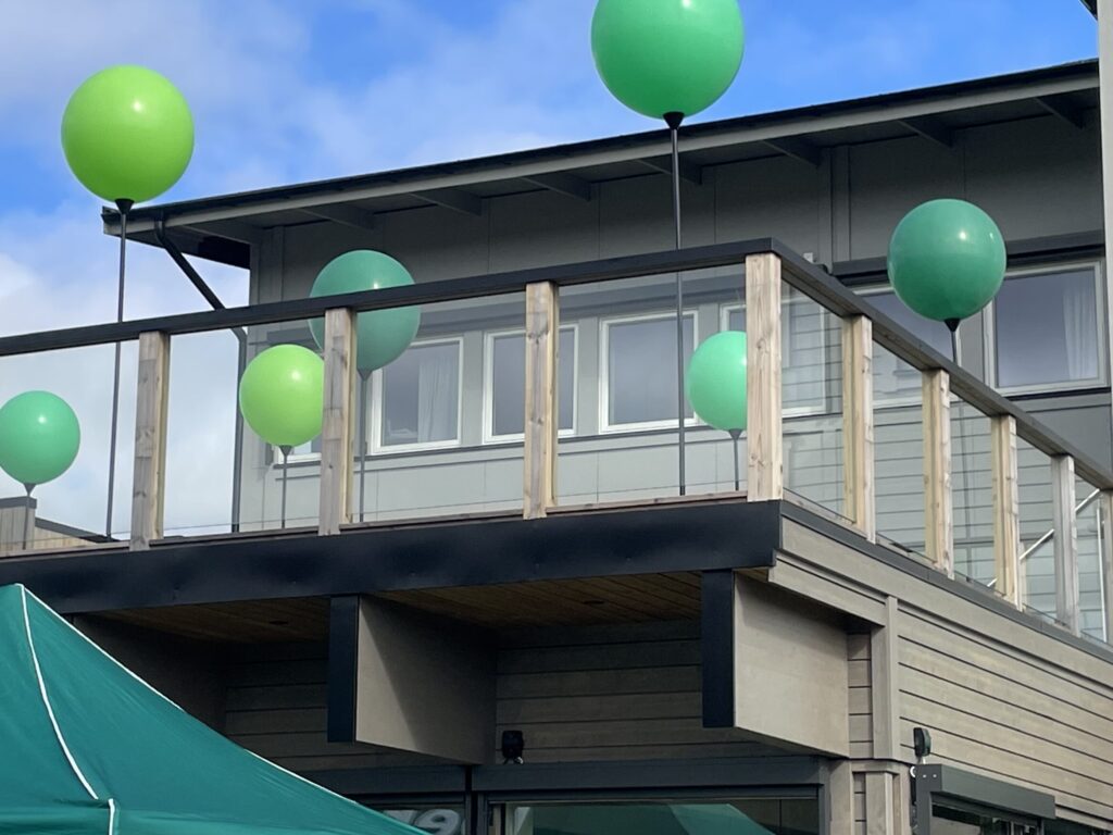 Grön ballongdekor med maxiloon-ballonger och organisk girlang vid invigning av Derome, på terrass och trappräcke.
